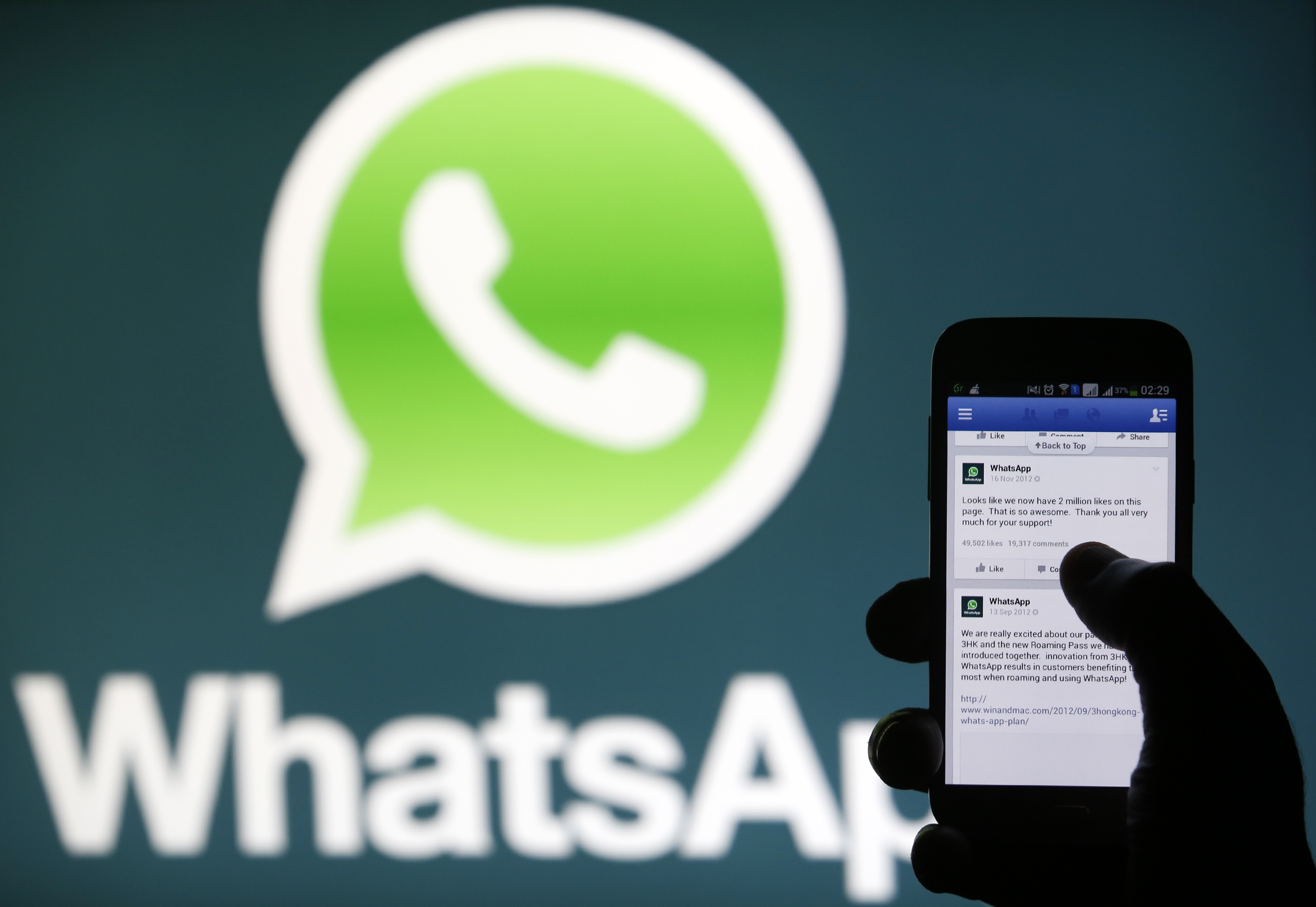 A Whatsapp App logo is seen behind a Samsung Galaxy S4 phone that is logged on to Facebook in the central Bosnian town of Zenica