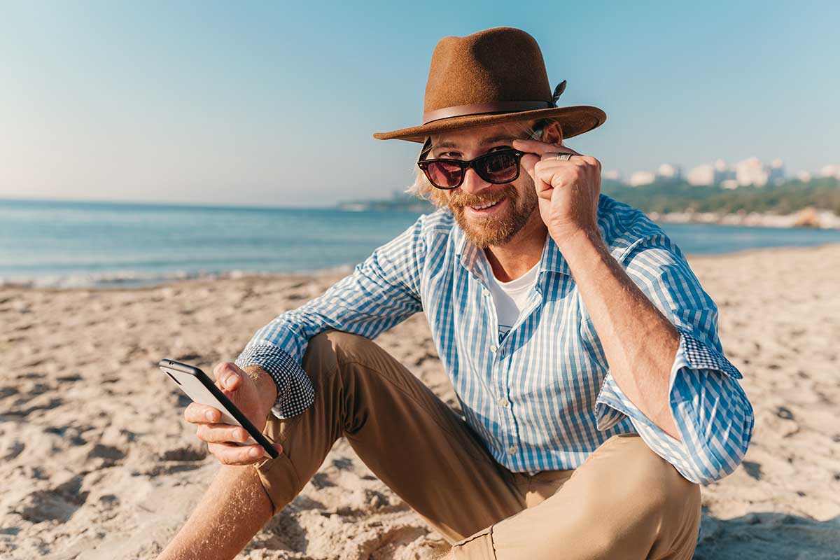Uomo in spiaggia con il cellulare in mano